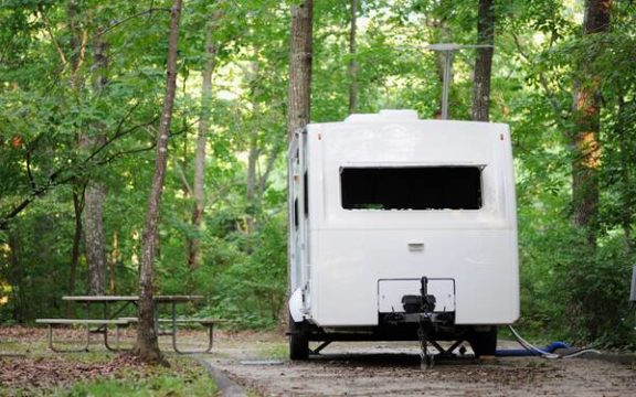 Travel trailer parked in the woods, next to a picnic table.