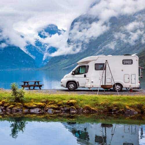 RV near lake and woods and mountains.