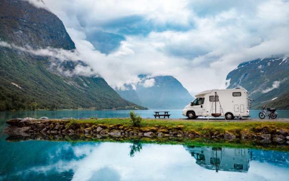 RV parked by a beautiful blue lake and mountains.