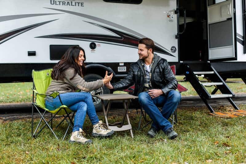 A smiling couple sitting in lawn chairs in front of an RV.