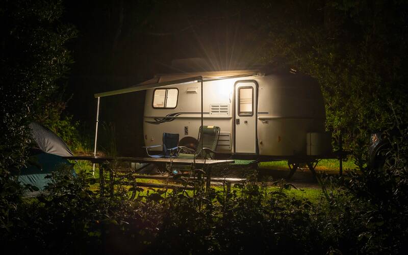 Camping trailer with porch light shining in the night.