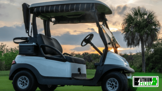 As the sun sets, a lithium-battery-powered golf cart sits parked in the field.