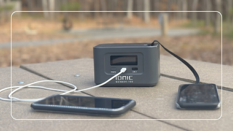 Ionic GenBox-100 portable power station charging two smartphones on an outdoor picnic table
