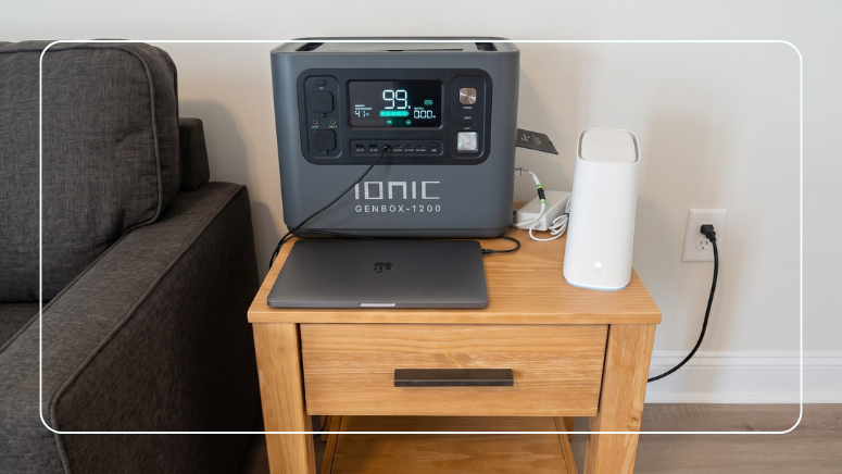 Ionic GenBox 1200 portable power station on a living room side table powering a laptop and home internet router