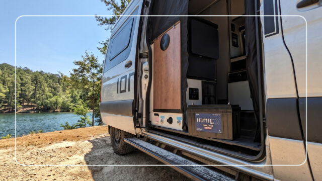 Ionic lithium RV battery and charger inside a camper van parked at a lakeside campsite