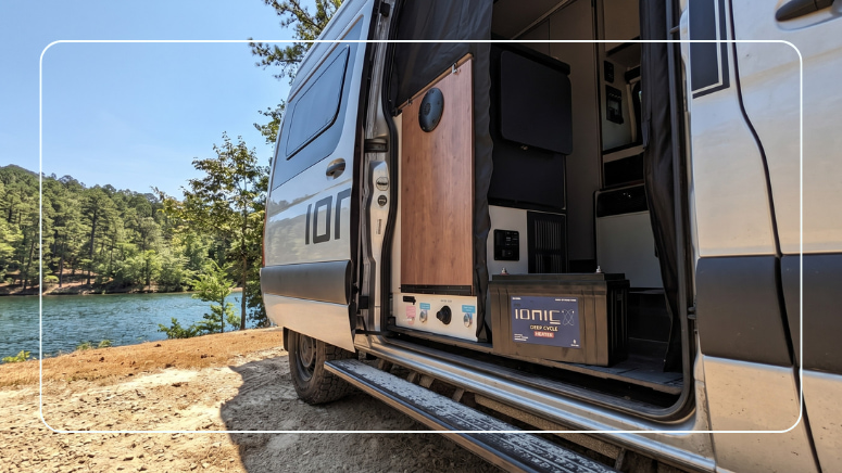 Ionic lithium RV battery and charger inside a camper van parked at a lakeside campsite