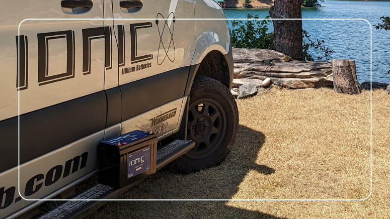 Ionic-branded camper van with a lithium RV battery parked by a lake for off-grid summer camping