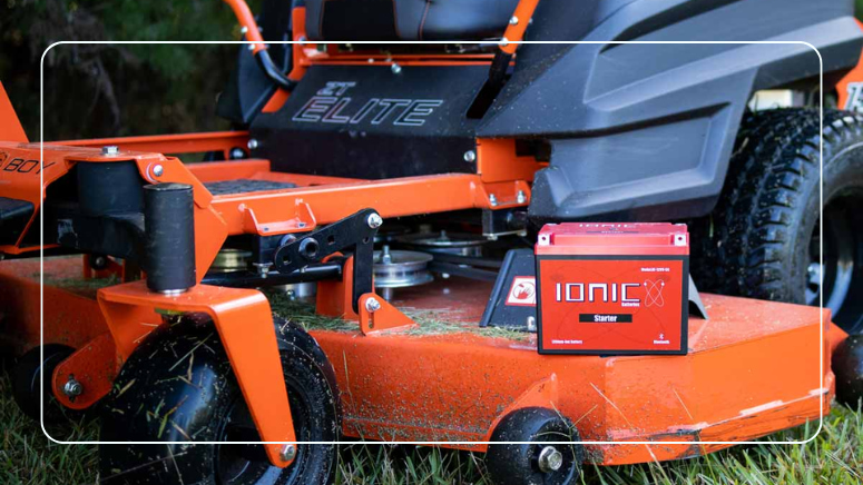 Red Ionic lithium starter battery on the deck of an orange zero-turn lawn mower