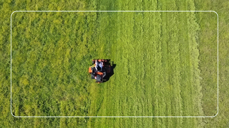 Aerial view of an orange zero-turn lawn mower cutting a green field