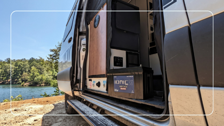 Ionic heated LiFePO4 deep cycle battery beside an RV power panel in an open camper van battery compartment