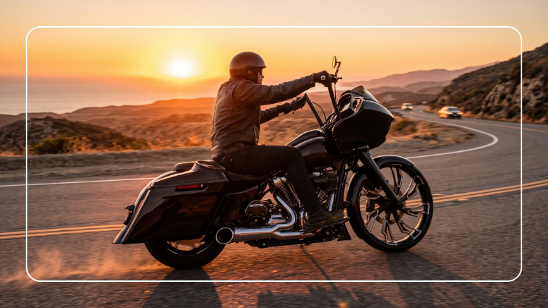 Rider on a black Harley-style touring motorcycle cruising a coastal highway at sunset
