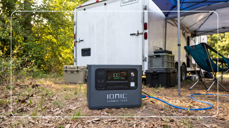 Ionic GenBox 1200 portable power station at a campsite beside a cargo trailer and canopy