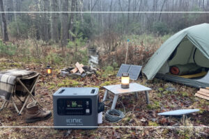 Ionic GenBox 2400 portable power station charging from a portable solar panel at a wooded campsite