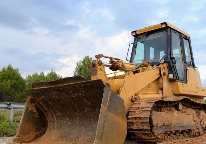 Big yellow bulldozer on the road beside leveled dirt.