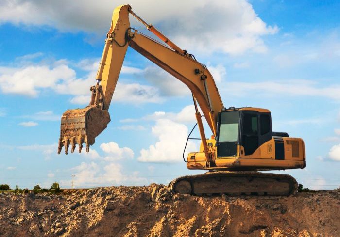 Large yellow excavator digging a huge hole in the ground.