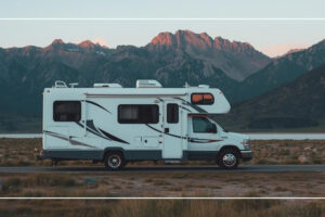 Class C motorhome parked on a desert road beside a lake with mountains at sunset