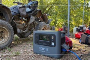 Ionic GenBox 1200 portable power station running at an outdoor trail site beside an ATV and gas fuel cans