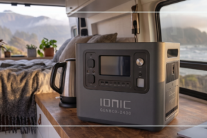 Ionic GenBox-2400 portable power station inside a camper van powering a kettle and laptop with a coastal ocean view through the window
