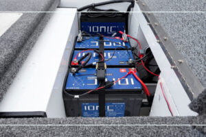 Ionic lithium deep cycle marine batteries wired and strapped inside a boat battery compartment with an Ionic on-board charger mounted above