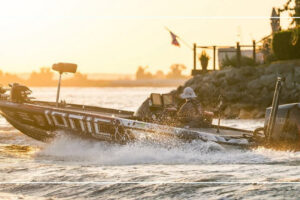 Angler driving an Ionic-wrapped bass boat across the water at sunset