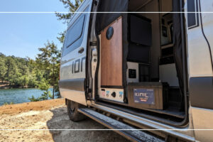 Ionic lithium RV battery and charger inside a camper van parked at a lakeside campsite