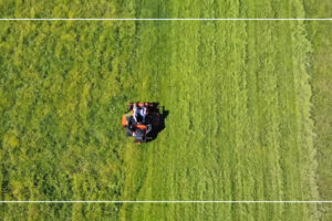 Aerial view of an orange zero-turn lawn mower cutting a green field