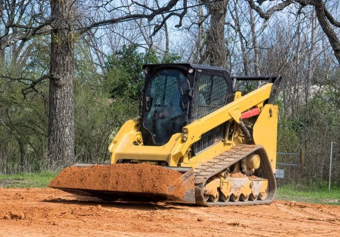 Yellow skid steer leveling ground, with trees in the background.
